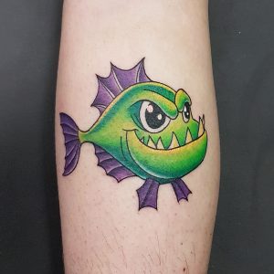 New school style tattoo of a green and purple fish with a smile and sharp teeth.