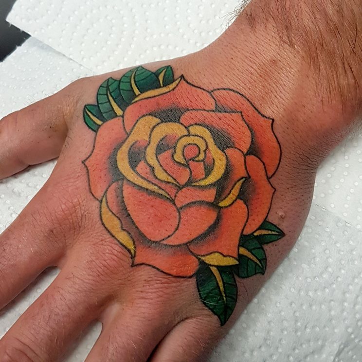 Traditional style orange rose with green leaves on hand.